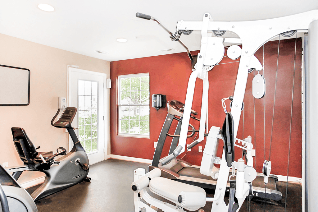 Fitness center with exercise equipment an entry door and window with a red accent wall