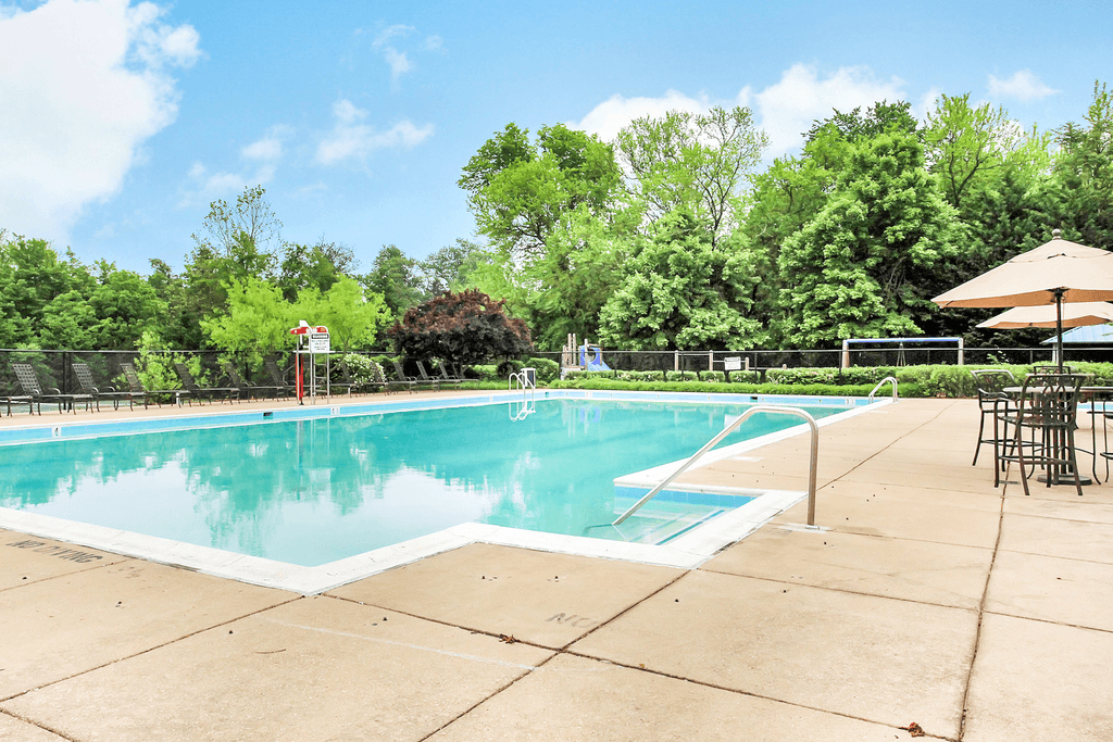 Swimming pool with large sun deck with tanning chairs and tables with umbrellas with playground and native landscape in the background