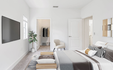 Bedroom facing a bed with a sitting chair and clothes hung up in the walk-in closet