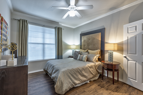 A bedroom with a bed, a ceiling fan, and a nightstand with a lamp.