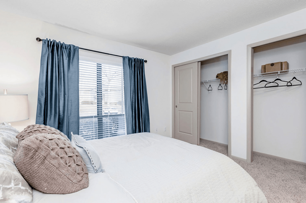 A bedroom with a large bed and a window with blue curtains at Madison Southpark Apartment Homes, Charlotte, NC, 28226