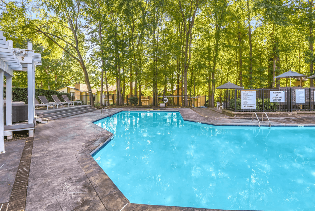 A pool surrounded by trees and a white pergola at Madison Southpark Apartment Homes, North Carolina, 28226