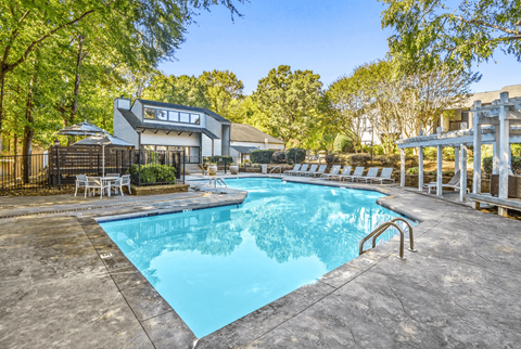 A swimming pool surrounded by trees and a house in the background.
