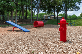 A red fire hydrant sits on a playground with a blue bench and two red barrels at Madison Southpark Apartment Homes, Charlotte, NC