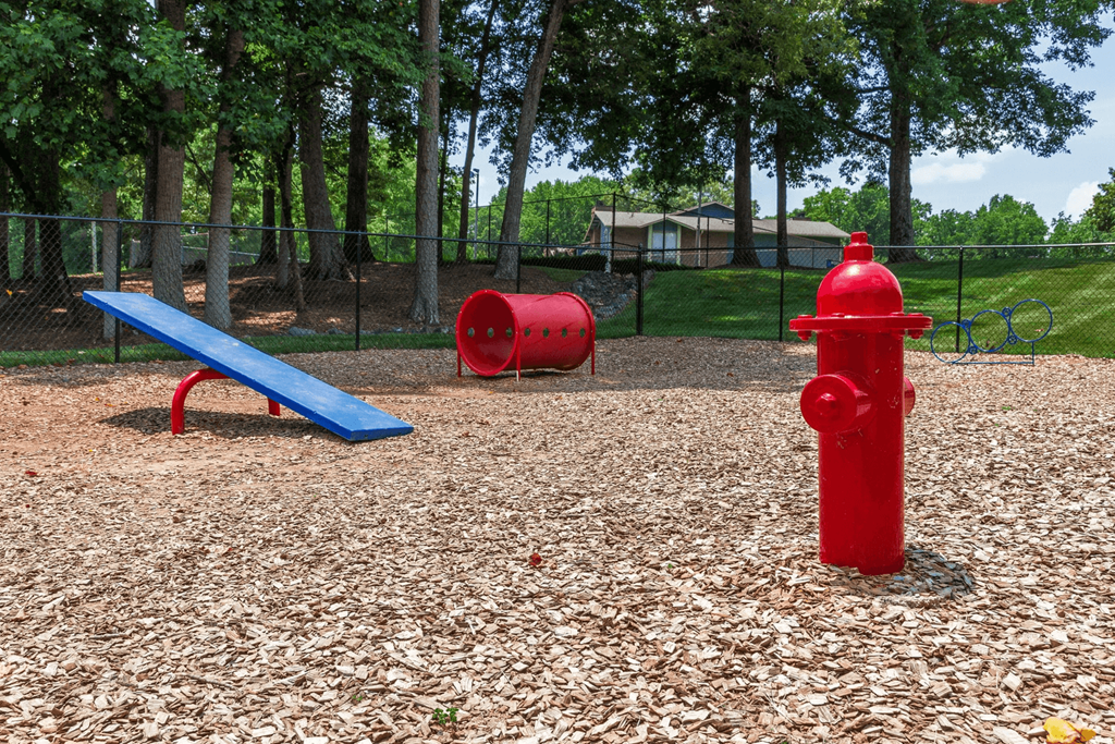 A red fire hydrant sits on a playground with a blue bench and two red barrels at Madison Southpark Apartment Homes, Charlotte, North Carolina