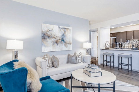 A blue chair with a white fur throw sits in a living room with a white couch and a large abstract painting on the wall.