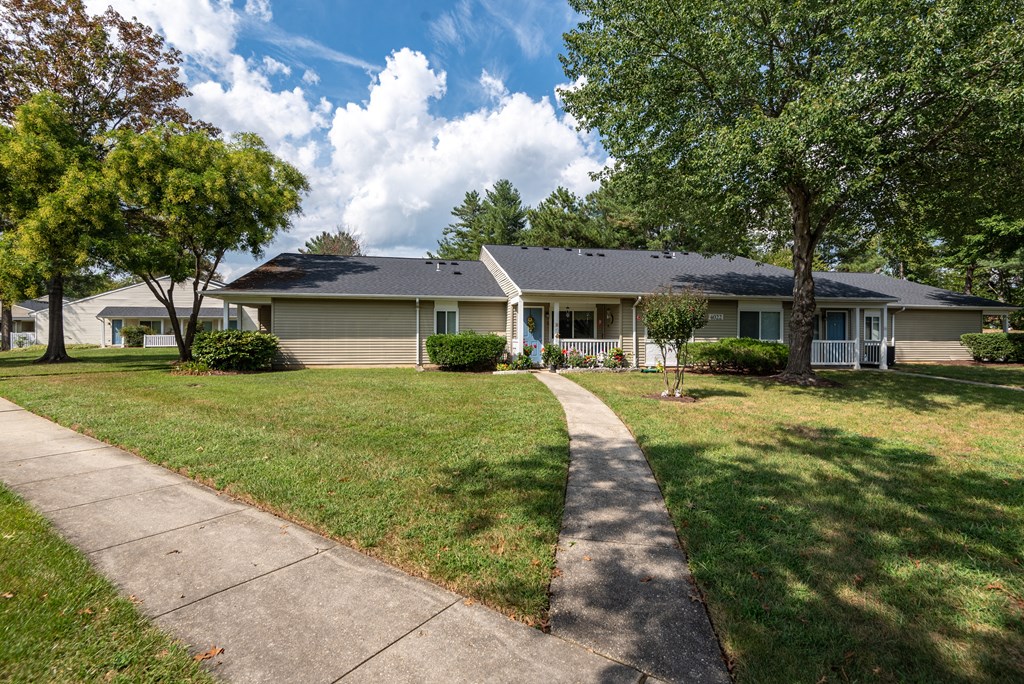 A house with a grey roof and a white fence is surrounded by green trees.