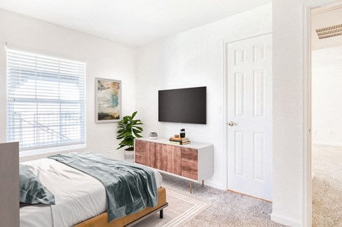 Model Bedroom with Bed Next to Window Next to Framed Wall Art Next to Plant, Dresser and Mounted TV
