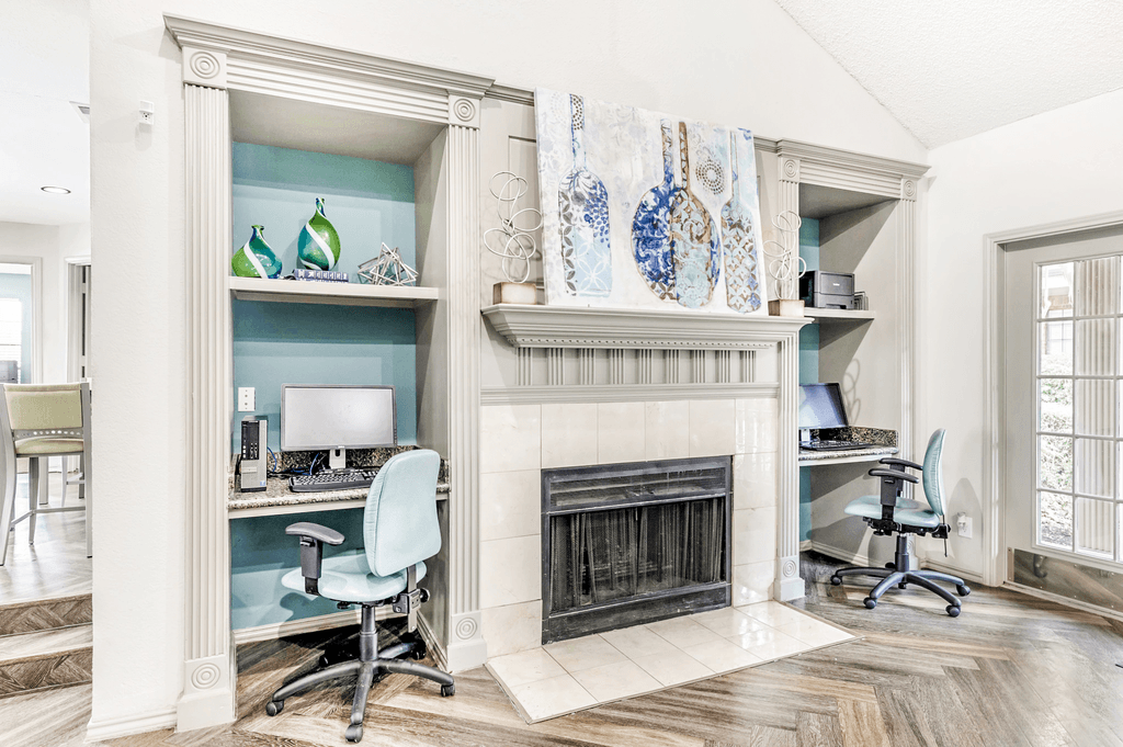Clubhouse interior and business center with built in desks with computers and chairs with fireplace in between and wood style flooring