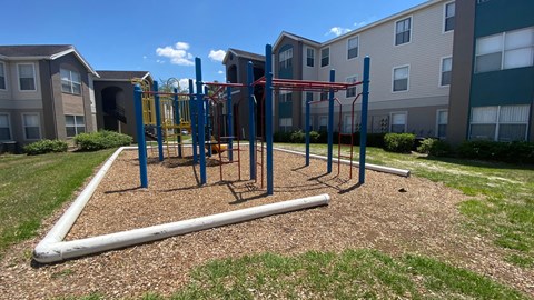 Red and blue playground set in a bed of mulch with building exteriors in the background