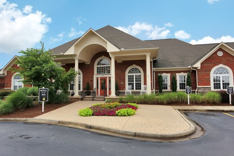 A red brick building with a large front porch and a sign on the lawn.