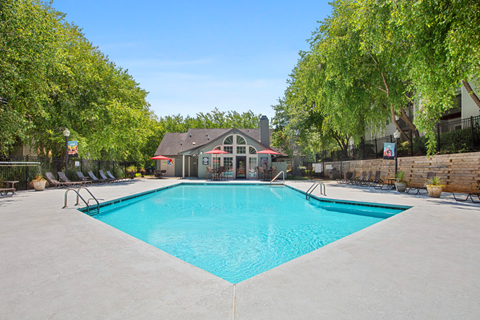 A large swimming pool surrounded by trees and a building in the background.