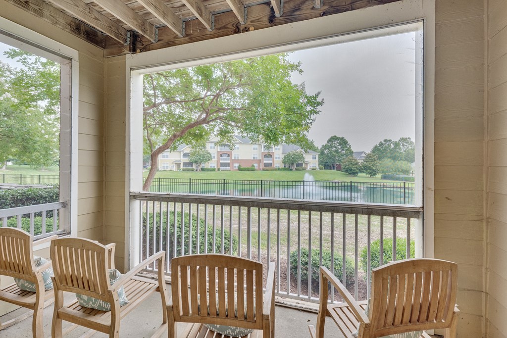 A balcony with four chairs and a view of a green lawn and trees.