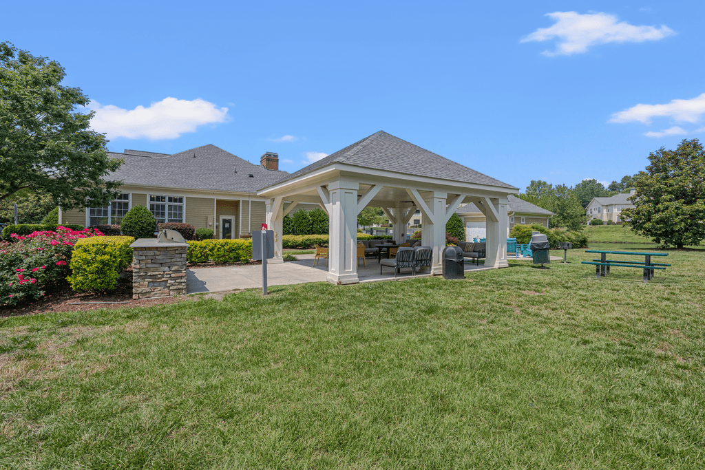 A gazebo is surrounded by a well-kept lawn and a stone wall.