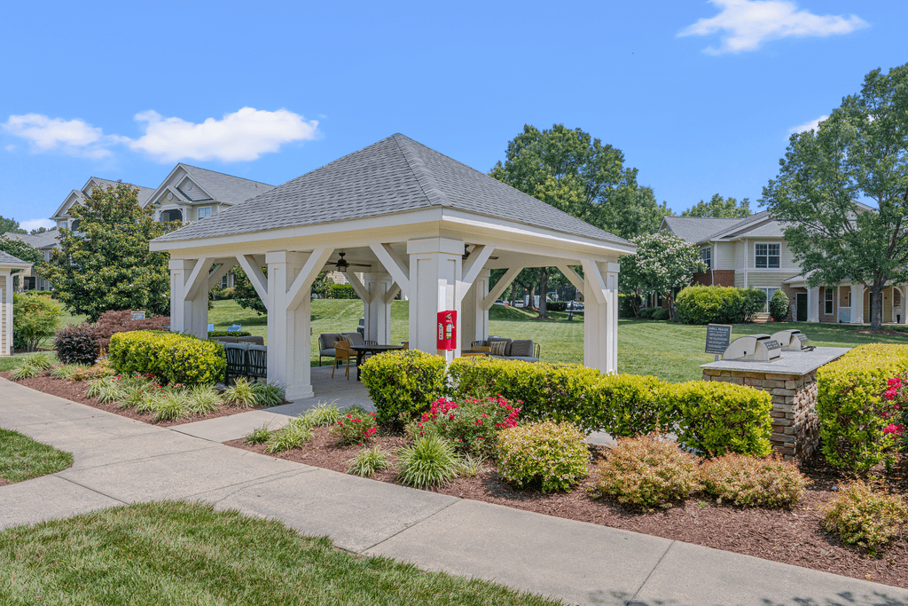 A gazebo is surrounded by bushes and flowers in a residential area.