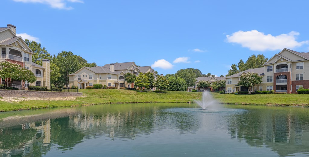 A serene lake in front of a row of houses with a fountain in the middle.