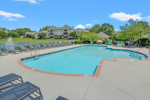 A large swimming pool surrounded by lounge chairs and trees.