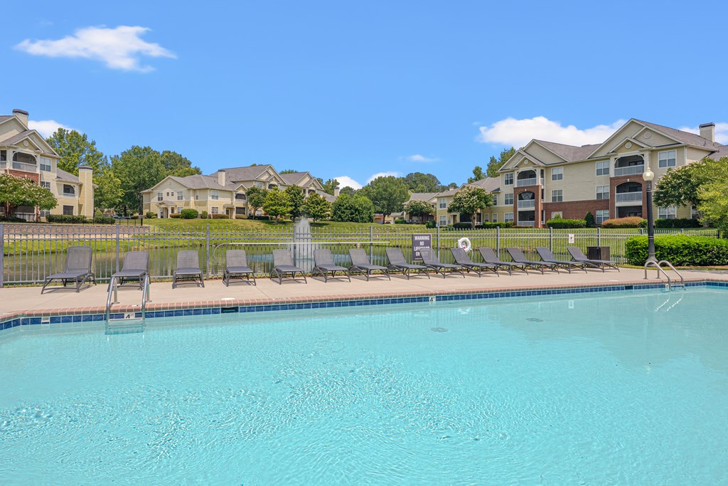 A swimming pool with lounge chairs and a row of houses in the background.