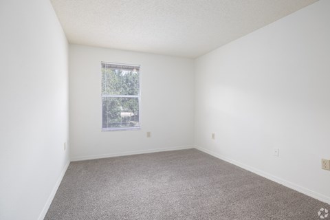 A room with a carpeted floor and a window with blinds.