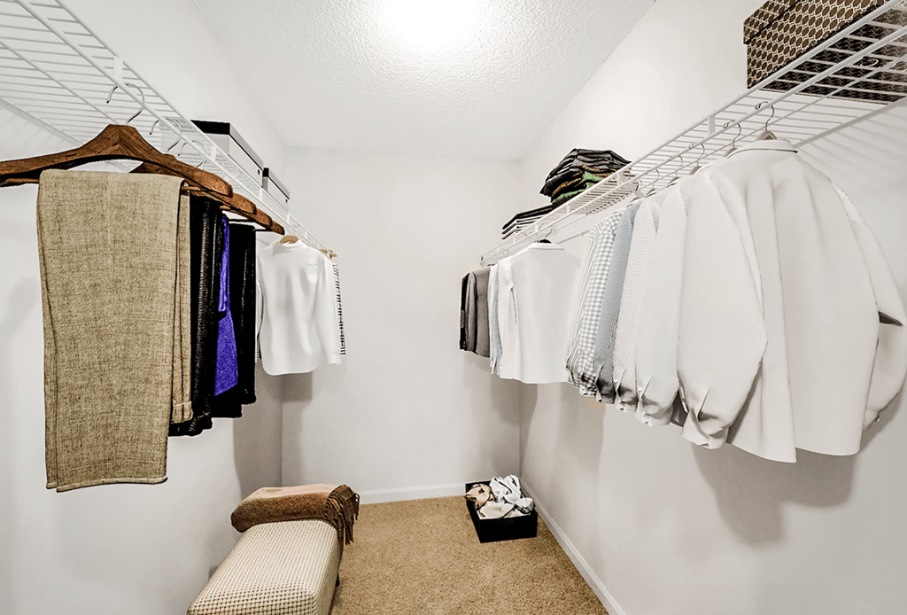 a walk in closet with white clothes hanging on the wall and a white bench in the corner