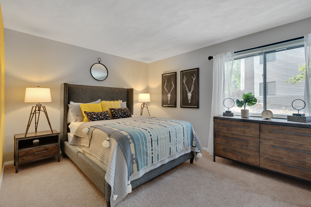 A bedroom with a bed, nightstand, and a window with a view of a tree.