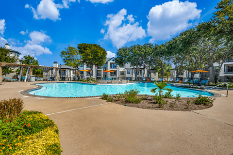 A large swimming pool surrounded by a sandy area and green plants.