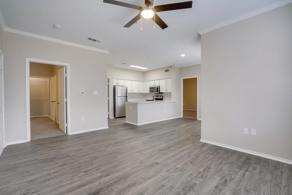 an empty living room with a ceiling fan and a kitchen