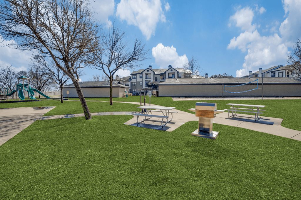 a park with picnic tables and a water fountain in front of a building