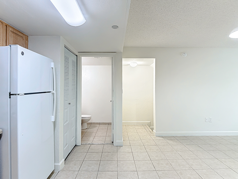 A white refrigerator is in a kitchen with white walls and tile flooring.