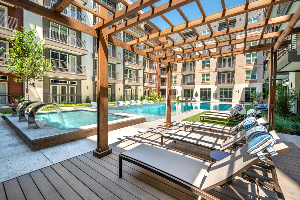 Swimming pool with lounge chairs under pergola, water fountain feature in wading pool with building exterior surrounding