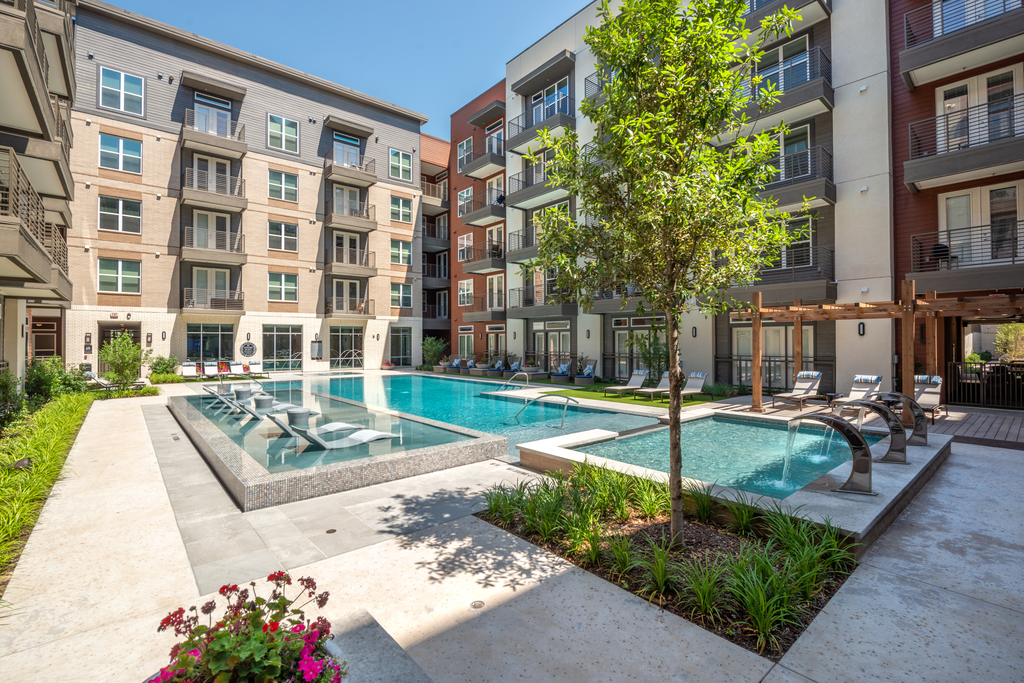 Zero edge swimming pool with heated spa, tanning shelf, lounge chairs, pergolas and building exterior surrounding