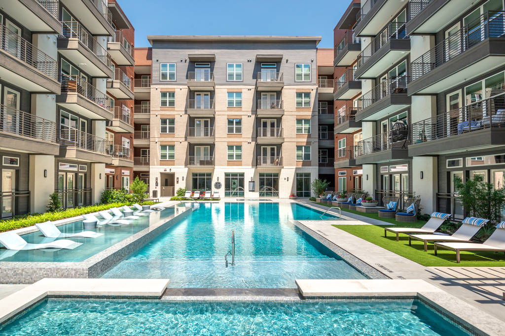 Zero edge swimming pool with heated spa, tanning shelf, lounge chairs, pergolas and building exterior surrounding