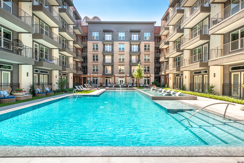 Zero edge swimming pool with tanning shelf, lounge chairs, pergolas and building exterior surrounding