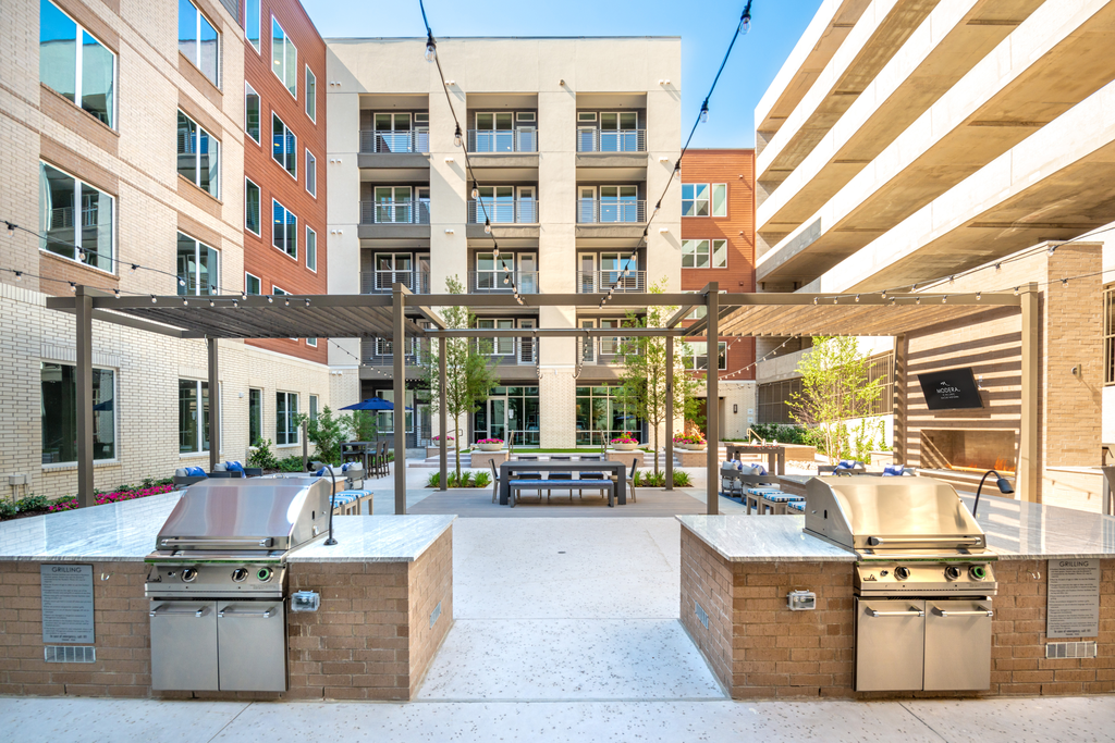 Outdoor grill area in courtyard with gas grills, pergola, hanging lights and alfresco dining