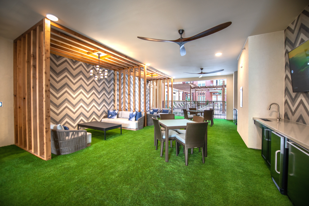 Private outdoor lounge with large ceiling fans, couches, wall mounted television, wet bar with mini fridge