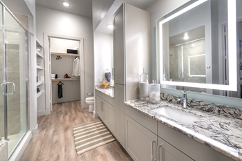 Staged bathroom with granite countertops, dual vanities, custom lighted vanity mirrors, wood style flooring, built-in shelving and direct access to walk in closet