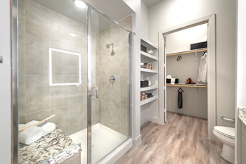 Staged bathroom with wood style flooring. walk in shower with granite bench, built in shelving, and direct access to walk in closet
