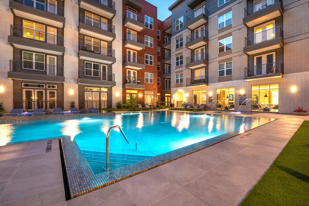 Zero edge swimming pool with fountains, tanning shelf and building exterior surrounding