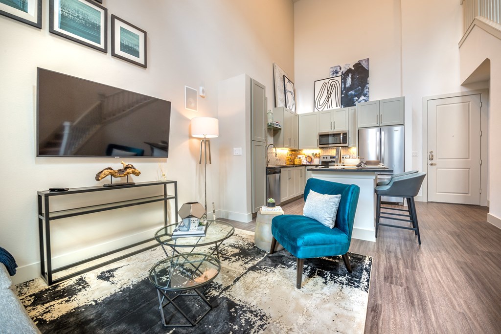 Living room area facing the kitchen and a television next to a blue velvet chair.