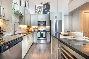 Kitchen with black quartz countertops and stainless steel appliances facing the sink and wine cooler.