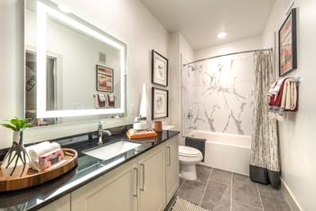 Bathroom facing sink with white cabinets, quartz countertops, and nickel brushed hardware with a lighted mirror.