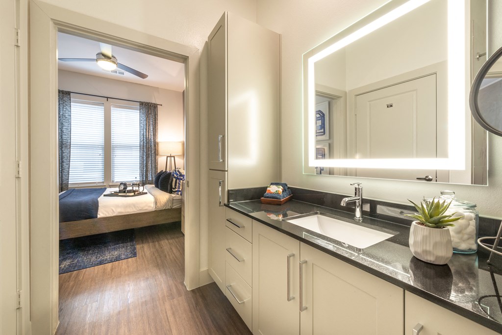 Interior bathroom featuring a back-lit mirror, quartz countertops, and brushed nickel hardware.
