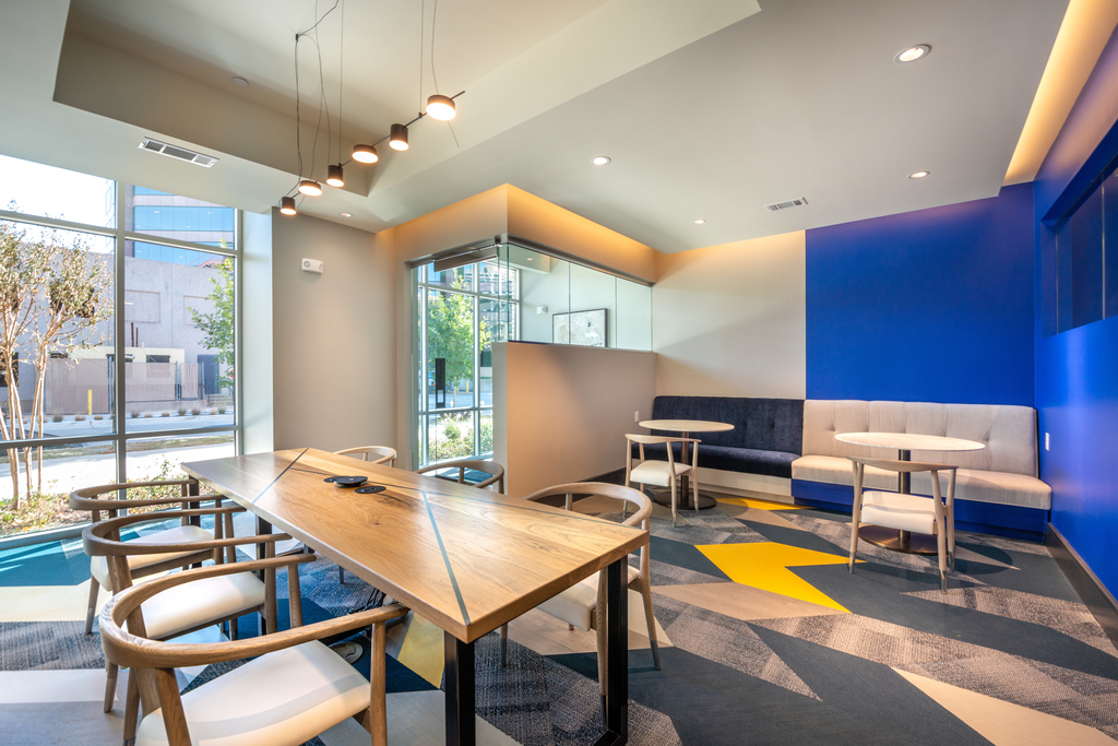 Clubhouse lounge with wall couch, table and chairs and a long wood table and chairs with recharge station