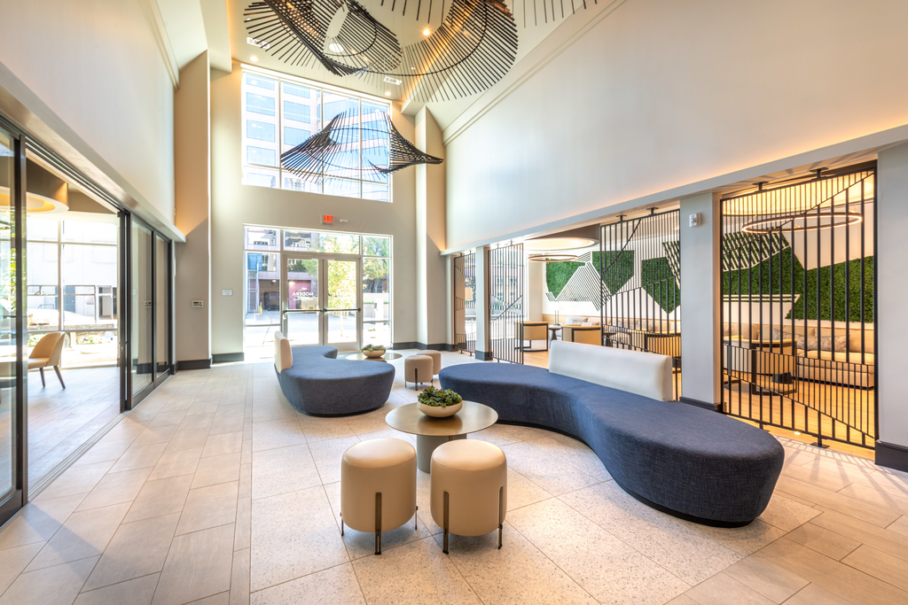 Clubhouse interior with uniquely shaped blue couches, gold table tops, white stools, and and large hanging fixtures