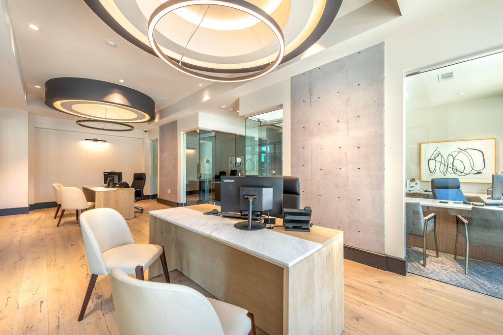 Leasing office interior with light wood desks, computers, chairs, and large circular designer hanging light with wood style flooring