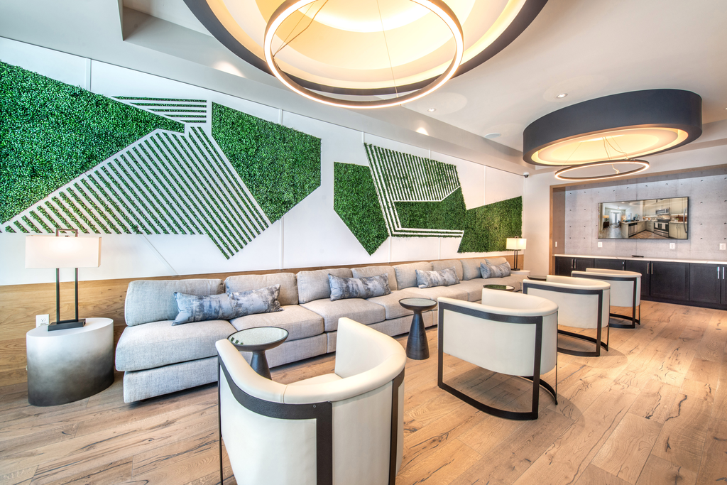 Clubhouse lounge with long couch and chairs with unique green wall art and large circular light fixtures with wall mounted television