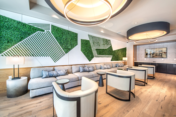 Clubhouse lounge with long couch and chairs with unique green wall art and large circular light fixtures with wall mounted television - Photo Gallery 23