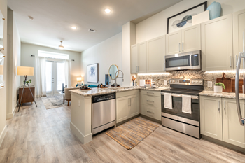 Staged kitchen with granite countertops, taupe cabinetry, stainless appliances, gooseneck faucet and living room in background - Photo Gallery 32