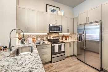 Staged kitchen with stainless appliances, granite countertops, goose neck faucet, taupe shaker cabinets, glass top stove and wood style flooring - Photo Gallery 31