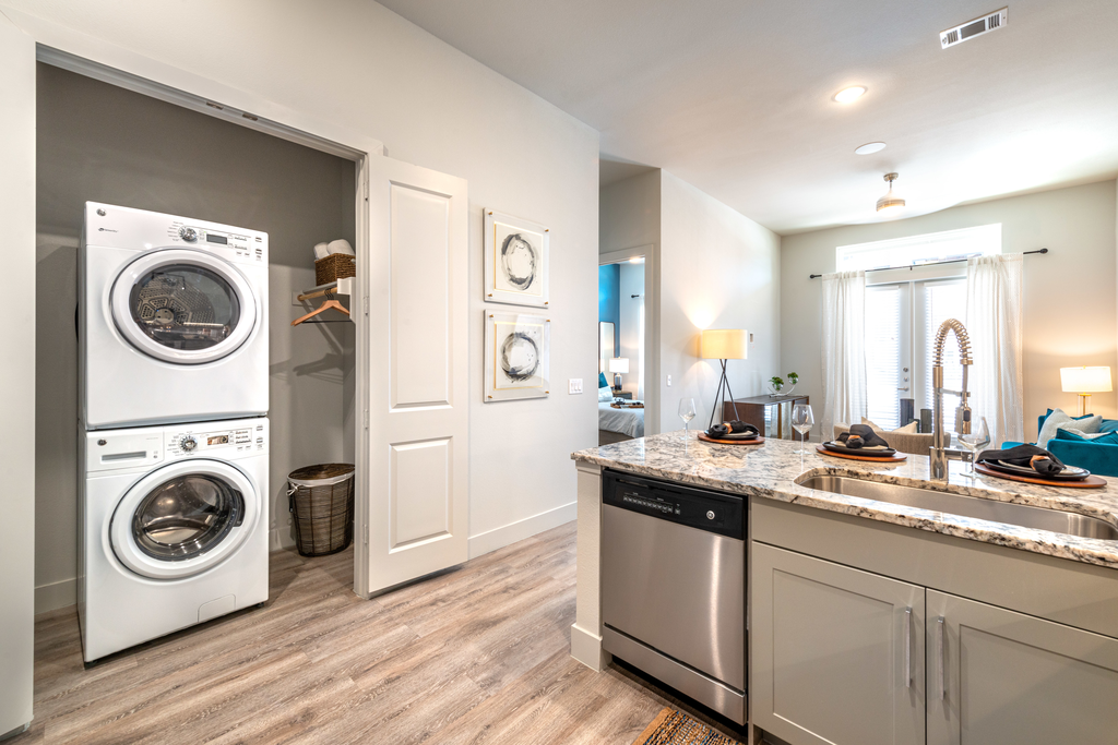 Laundry area with front loading stacked washer and dryer with clothes rack and shelf off kitchen